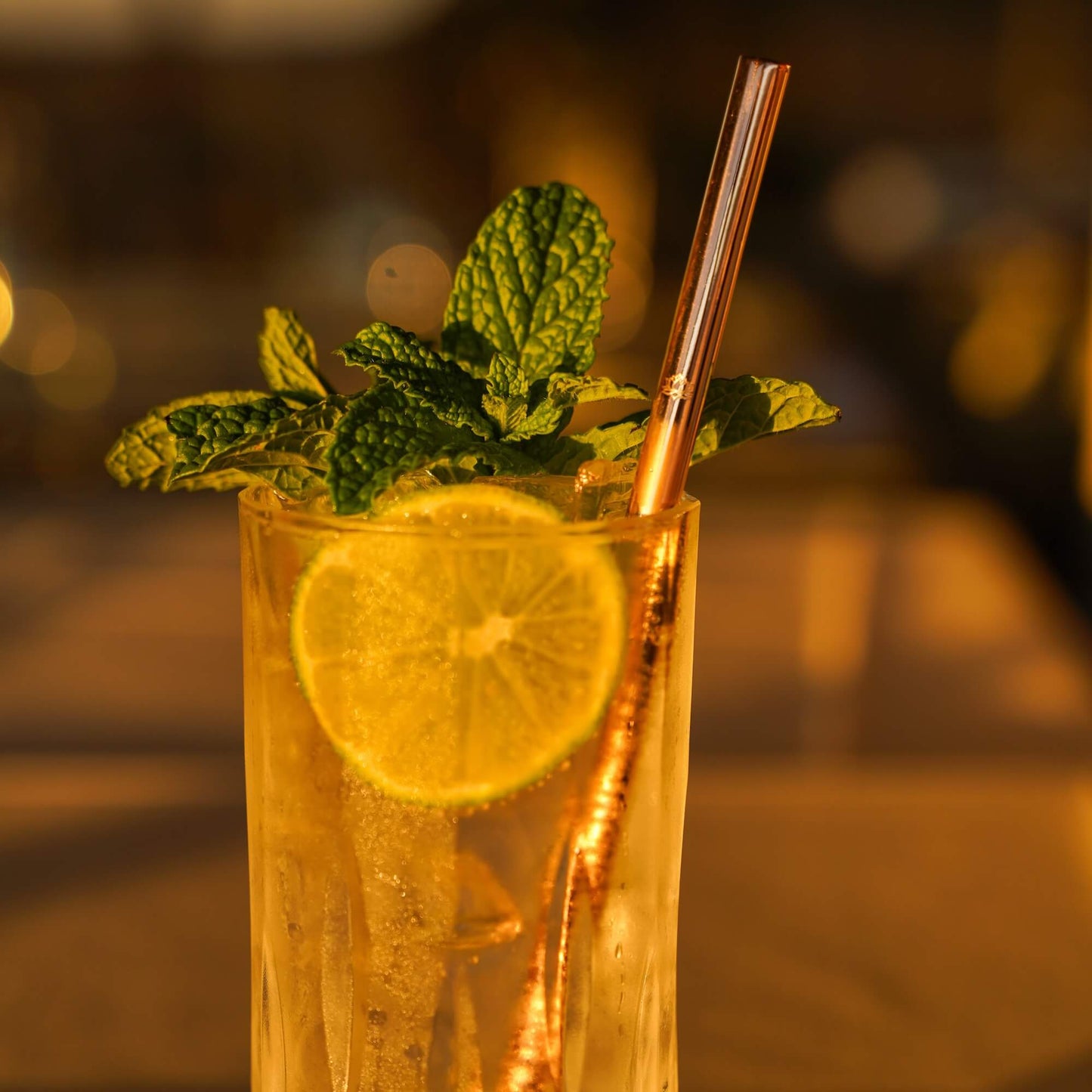 Amber-colored iced tea with rose gold metal straw and lemon slice garnish in tall glass