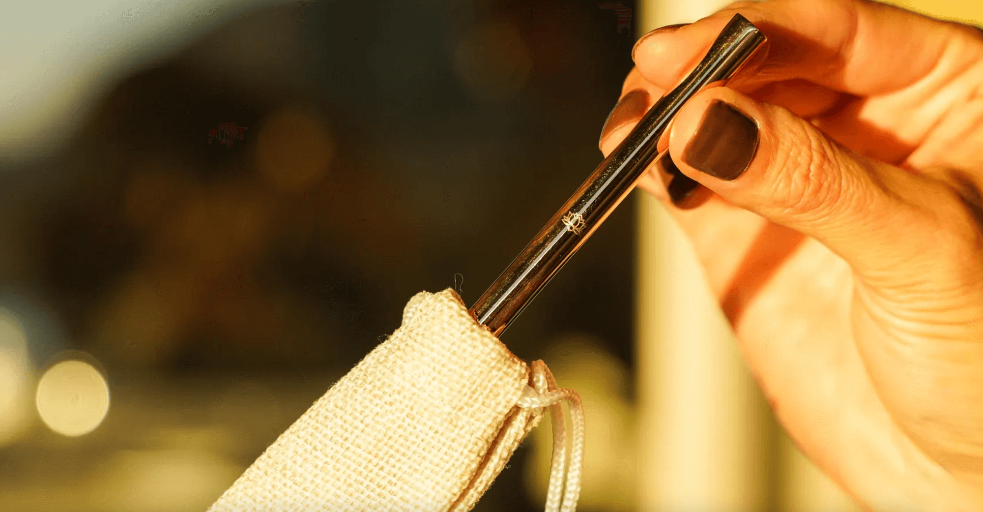 Hand using gold metal straws to drink from coconut with woven holder, demonstrating Ecolux's eco-friendly Sipper Collection