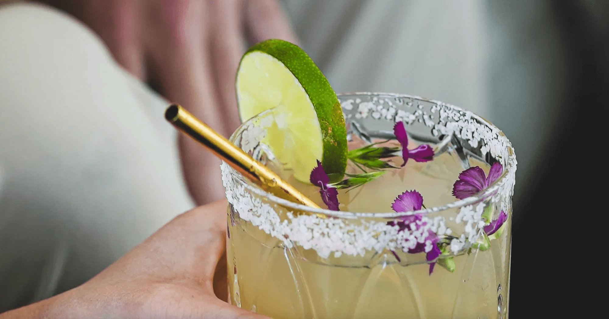Margarita cocktail with salt rim, lime garnish and purple edible flowers, featuring gold metal straw from Ecolux's Sipper Collection