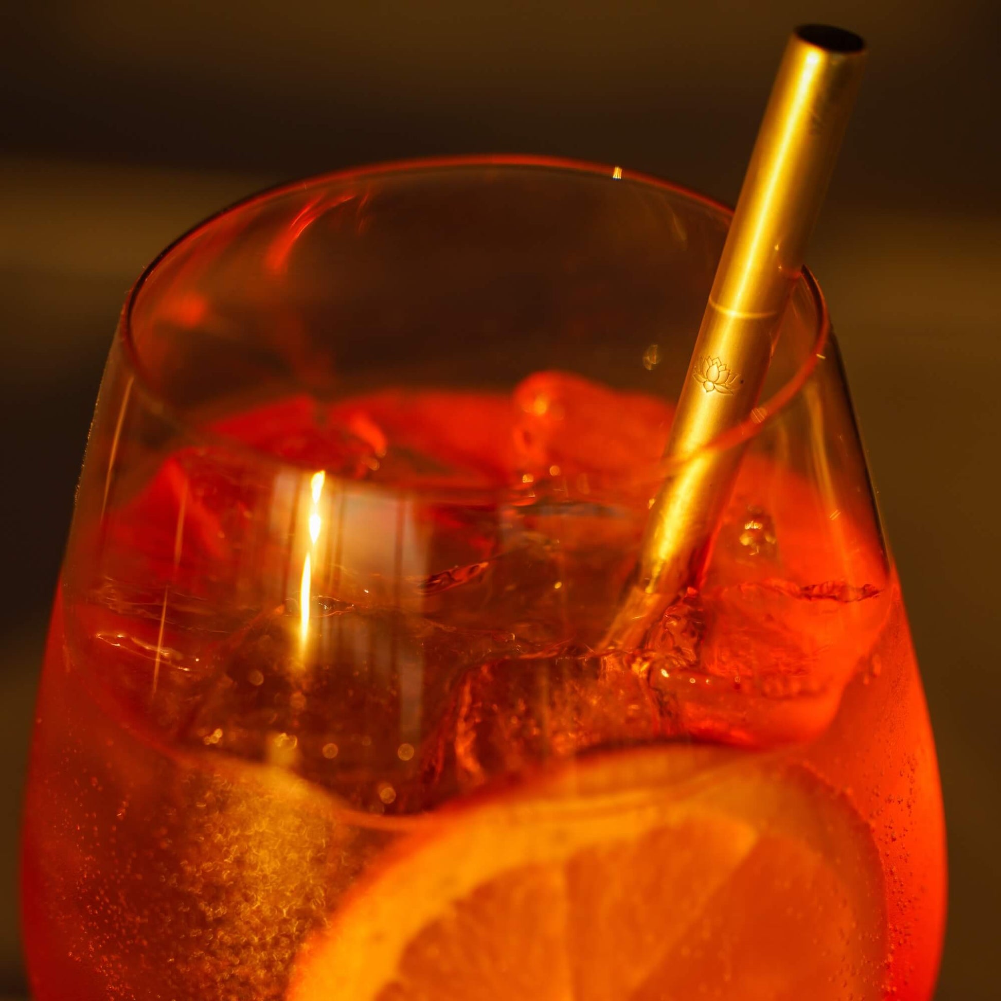 Red cocktail in glass with gold metal straw, lit candle visible in background