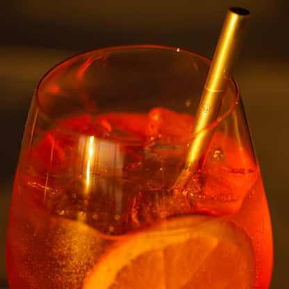 Red cocktail in glass with gold metal straw, lit candle visible in background